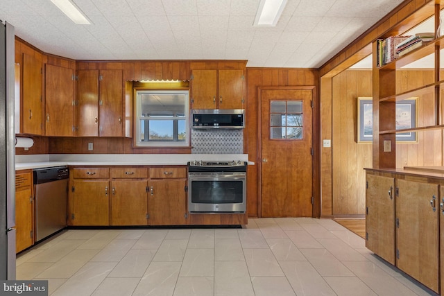 kitchen featuring decorative backsplash, wood walls, a healthy amount of sunlight, and appliances with stainless steel finishes