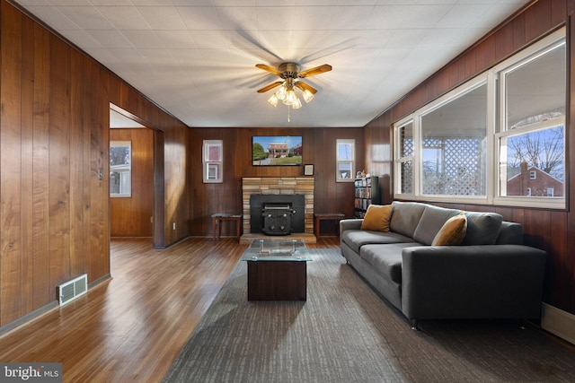 living room with ceiling fan, wood-type flooring, and wood walls