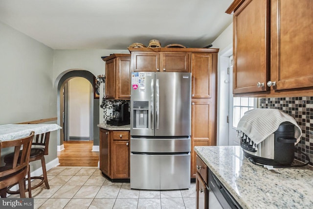 kitchen with stainless steel refrigerator with ice dispenser, light tile patterned flooring, light stone counters, and backsplash