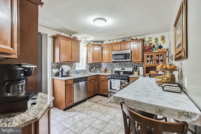 kitchen with sink, light stone counters, light tile patterned floors, stainless steel appliances, and backsplash