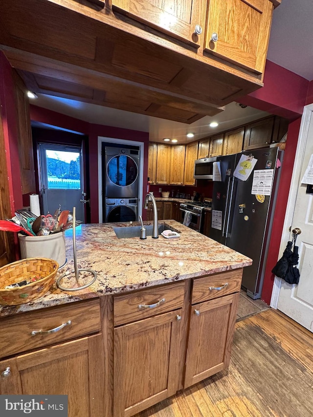 kitchen featuring stacked washer / dryer, sink, light stone counters, light hardwood / wood-style floors, and stainless steel appliances