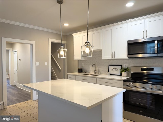 kitchen with appliances with stainless steel finishes, a kitchen island, white cabinetry, sink, and hanging light fixtures