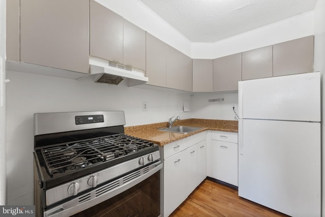 kitchen with stainless steel range with gas cooktop, sink, light wood-type flooring, white fridge, and a textured ceiling