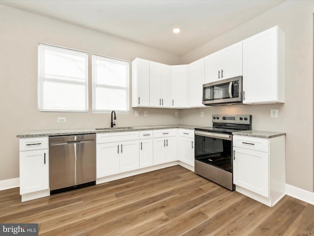 kitchen featuring sink, white cabinetry, light wood-type flooring, stainless steel appliances, and light stone countertops