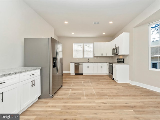 kitchen featuring white cabinetry, stainless steel appliances, light stone counters, and light hardwood / wood-style flooring