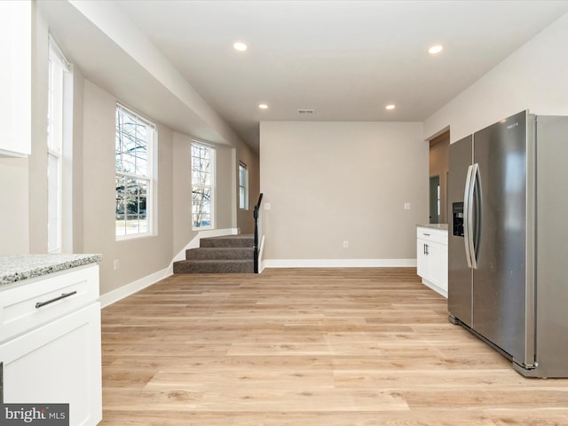 kitchen with white cabinetry, stainless steel fridge with ice dispenser, light stone countertops, and light hardwood / wood-style floors