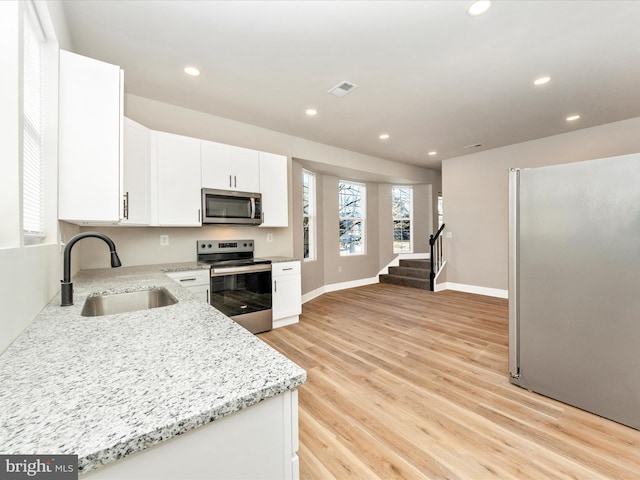 kitchen with appliances with stainless steel finishes, sink, white cabinets, light stone counters, and light hardwood / wood-style floors