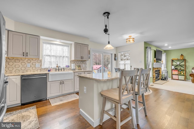 kitchen featuring sink, a center island, hanging light fixtures, stainless steel dishwasher, and light stone countertops