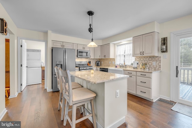 kitchen featuring a kitchen island, appliances with stainless steel finishes, pendant lighting, hardwood / wood-style flooring, and light stone counters