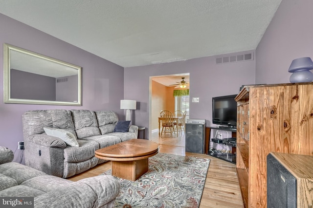 living room featuring ceiling fan, light hardwood / wood-style floors, and a textured ceiling