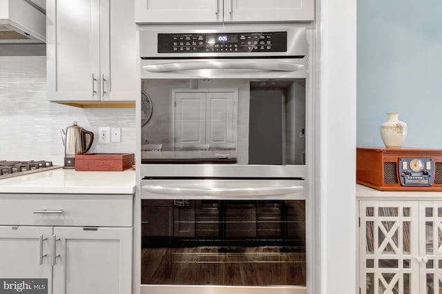 kitchen with backsplash, double oven, custom range hood, and white cabinets