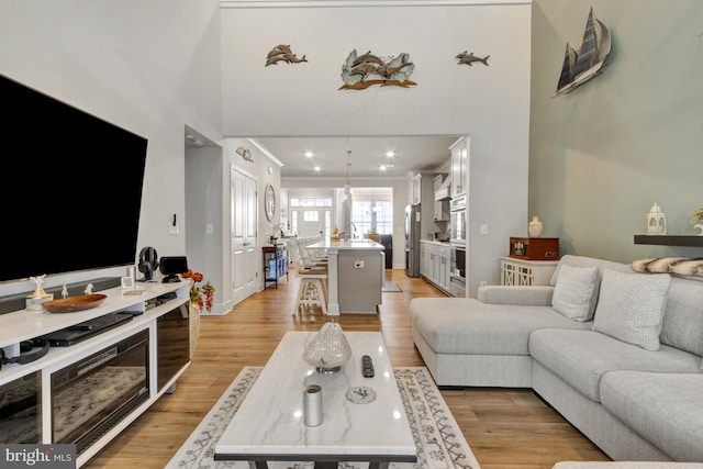 living room featuring sink, ornamental molding, light hardwood / wood-style floors, and a high ceiling