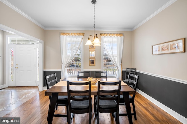 dining space featuring wood-type flooring, ornamental molding, and a notable chandelier