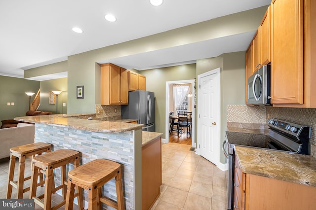 kitchen featuring a breakfast bar, appliances with stainless steel finishes, tasteful backsplash, light stone countertops, and kitchen peninsula