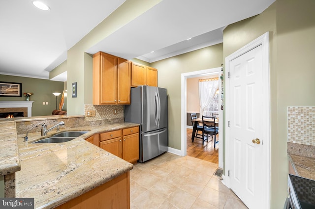 kitchen featuring sink, stainless steel fridge, kitchen peninsula, light stone countertops, and backsplash