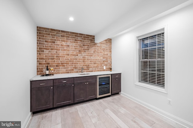 bar with wine cooler, sink, dark brown cabinets, brick wall, and light hardwood / wood-style floors