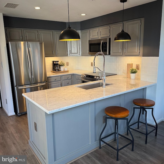 kitchen with pendant lighting, appliances with stainless steel finishes, dark hardwood / wood-style floors, and kitchen peninsula