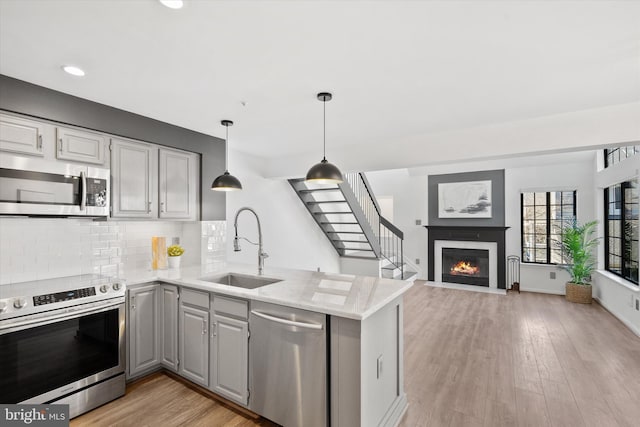 kitchen featuring sink, gray cabinetry, hanging light fixtures, stainless steel appliances, and kitchen peninsula