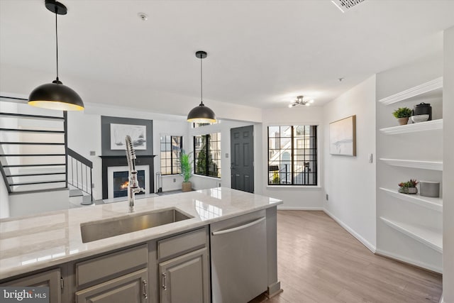 kitchen with pendant lighting, dishwasher, sink, light stone counters, and light hardwood / wood-style flooring