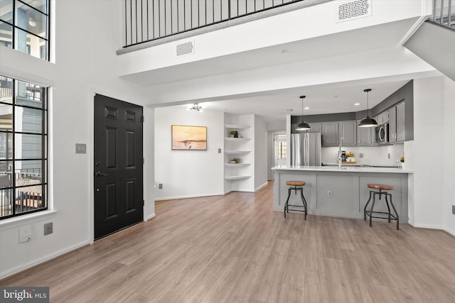 kitchen featuring appliances with stainless steel finishes, a breakfast bar area, gray cabinetry, kitchen peninsula, and light hardwood / wood-style flooring