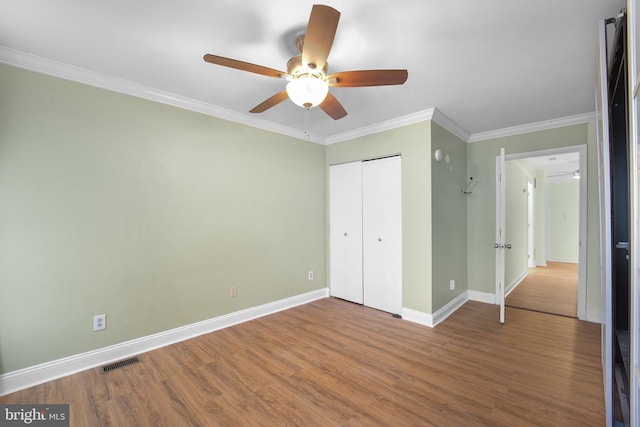 unfurnished bedroom with crown molding, wood-type flooring, a closet, and ceiling fan