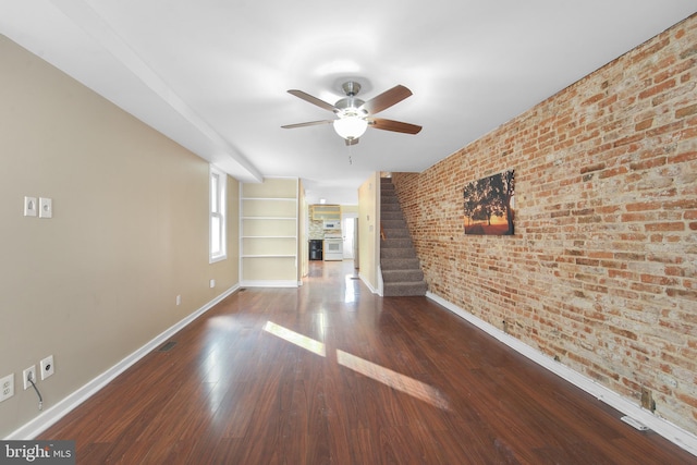 unfurnished living room with ceiling fan, brick wall, dark hardwood / wood-style flooring, and built in features