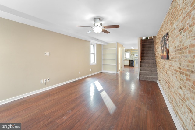 unfurnished living room with dark wood-type flooring, ceiling fan, and brick wall