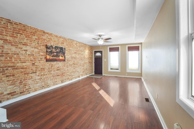 spare room featuring dark wood-type flooring, ceiling fan, and brick wall