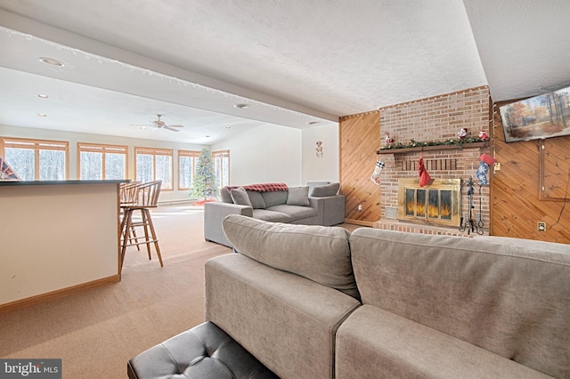 carpeted living room featuring ceiling fan, wooden walls, a brick fireplace, and a textured ceiling