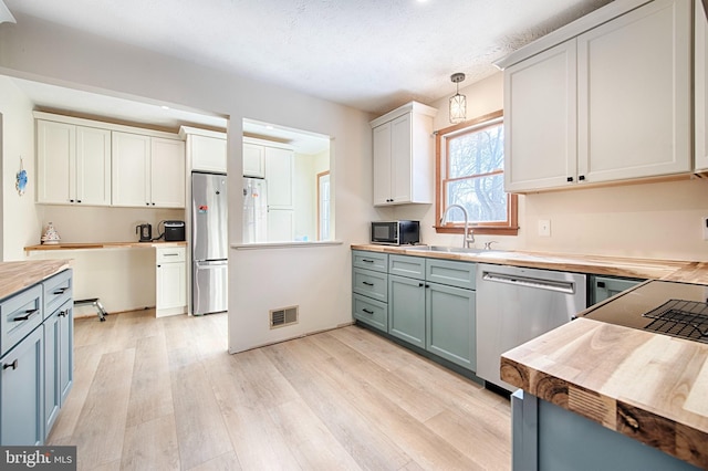 kitchen featuring pendant lighting, wood counters, sink, white cabinets, and stainless steel appliances