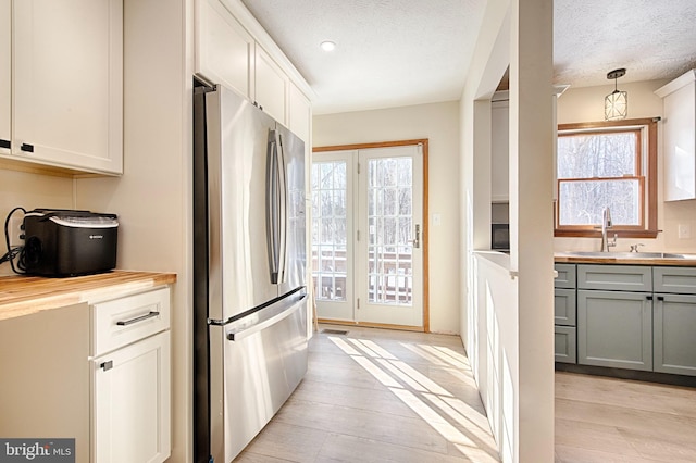 kitchen with wooden counters, hanging light fixtures, stainless steel refrigerator, gray cabinets, and a healthy amount of sunlight