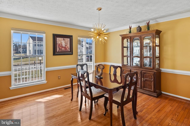 dining area featuring ornamental molding, a notable chandelier, a textured ceiling, and light hardwood / wood-style flooring