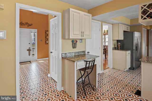 kitchen with dark stone countertops, stainless steel fridge with ice dispenser, white cabinetry, and a kitchen bar