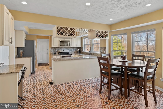 kitchen with sink, kitchen peninsula, stainless steel appliances, light stone countertops, and backsplash