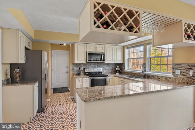 kitchen with stainless steel appliances, sink, light stone counters, and kitchen peninsula