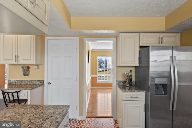 kitchen with dark stone countertops, stainless steel fridge with ice dispenser, and a textured ceiling