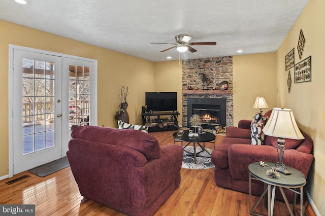 living room featuring french doors, a textured ceiling, light wood-type flooring, and a fireplace