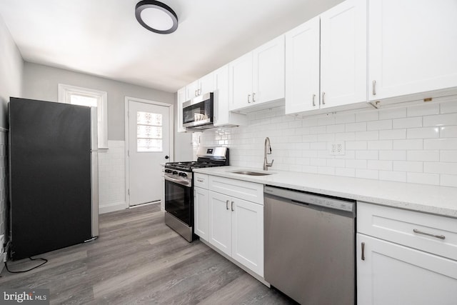 kitchen with sink, white cabinetry, light hardwood / wood-style flooring, appliances with stainless steel finishes, and light stone countertops