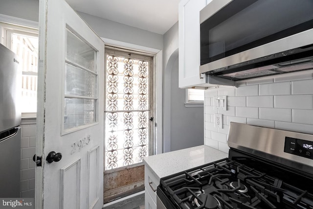 kitchen with tasteful backsplash, white cabinetry, appliances with stainless steel finishes, and light stone countertops