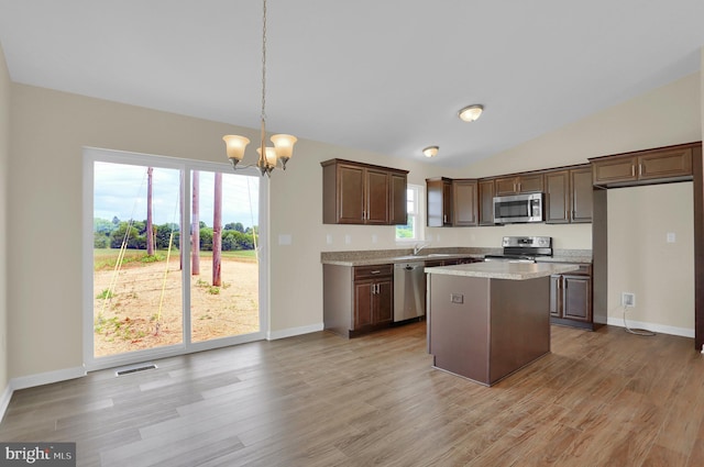 kitchen featuring a kitchen island, appliances with stainless steel finishes, decorative light fixtures, lofted ceiling, and light wood-type flooring