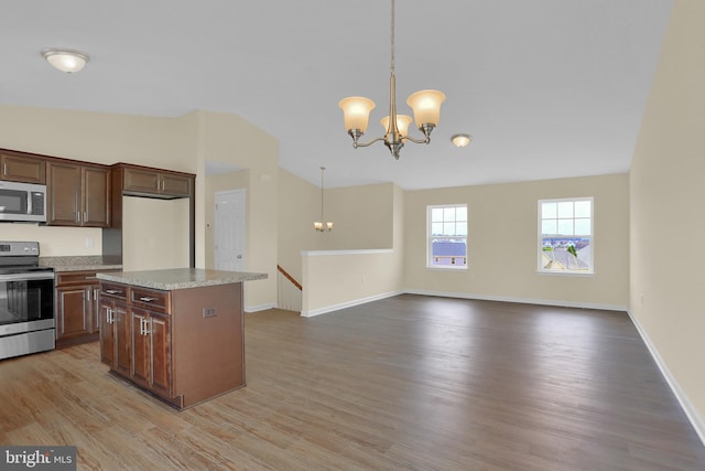 kitchen with light stone counters, decorative light fixtures, a chandelier, appliances with stainless steel finishes, and a kitchen island