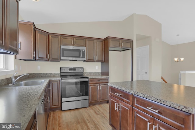 kitchen with lofted ceiling, sink, decorative light fixtures, stainless steel appliances, and light hardwood / wood-style floors