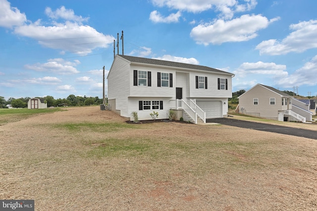 raised ranch featuring a garage, a front yard, and a storage unit