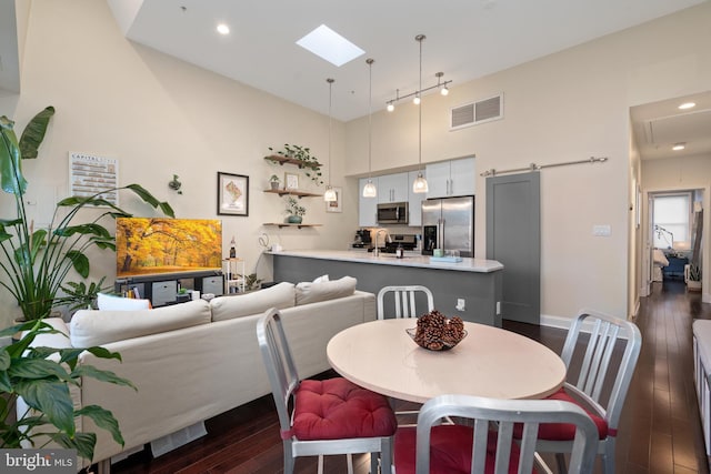 dining space featuring sink, dark wood-type flooring, a towering ceiling, a skylight, and a barn door