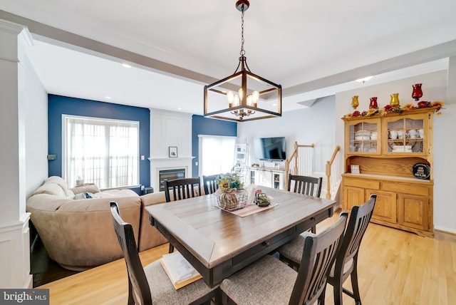 dining space with an inviting chandelier, crown molding, a fireplace, and light hardwood / wood-style floors