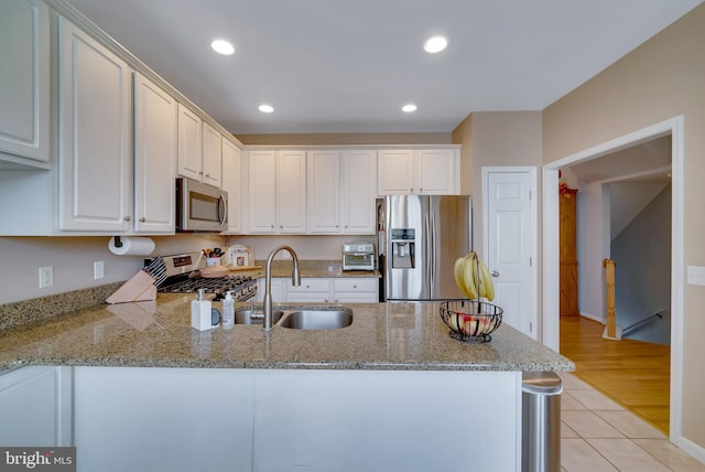 kitchen with sink, kitchen peninsula, stainless steel appliances, light stone countertops, and white cabinets