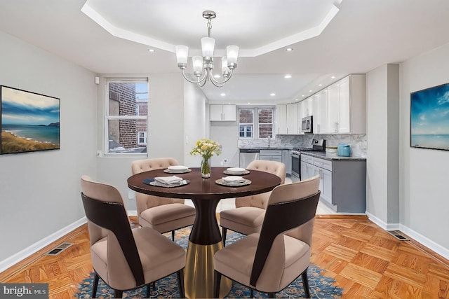 dining room featuring light parquet flooring, a tray ceiling, and a notable chandelier