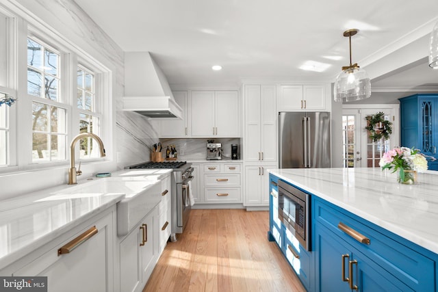 kitchen featuring blue cabinets, high end appliances, white cabinetry, custom range hood, and light stone countertops