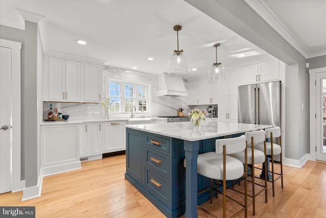 kitchen with custom exhaust hood, white cabinetry, a center island, hanging light fixtures, and high quality fridge