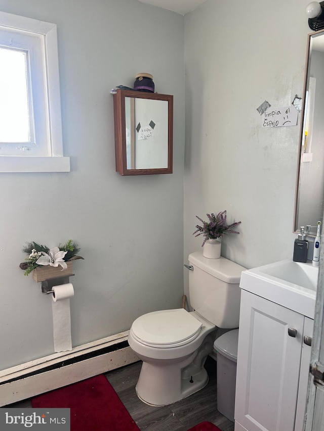 half bath with a baseboard heating unit, toilet, wood finished floors, and vanity